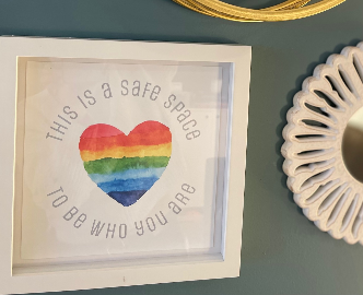 Framed rainbow watercolor heart reading "This is a safe space to be who you are"