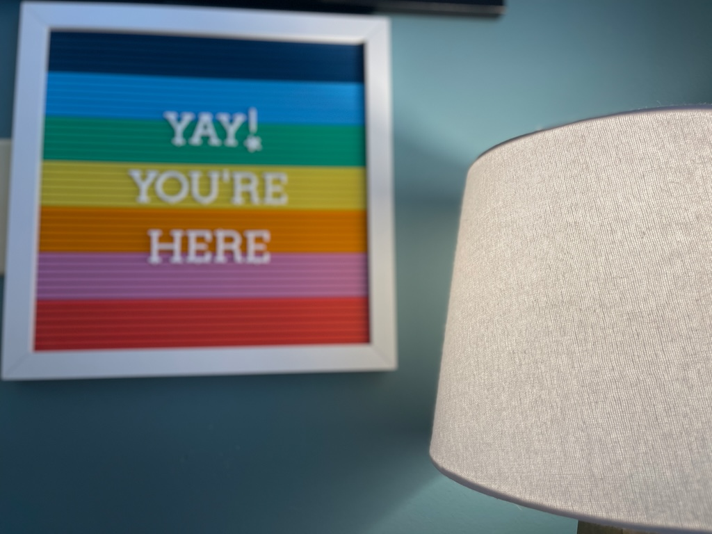 Rainbow-striped framed print reading "Yay! You're here" beside a lamp