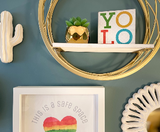 Framed print reading "This is a safe space" with a rainbow watercolor heart, on a shelf with a small succulent