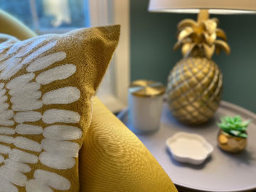 Cozy office corner with a mustard throw pillow, a gold pineapple lamp, and a candle