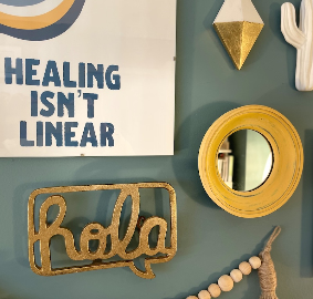 Office wall art reading "Healing isn't linear," with a gold "hola" sign and a small round mirror